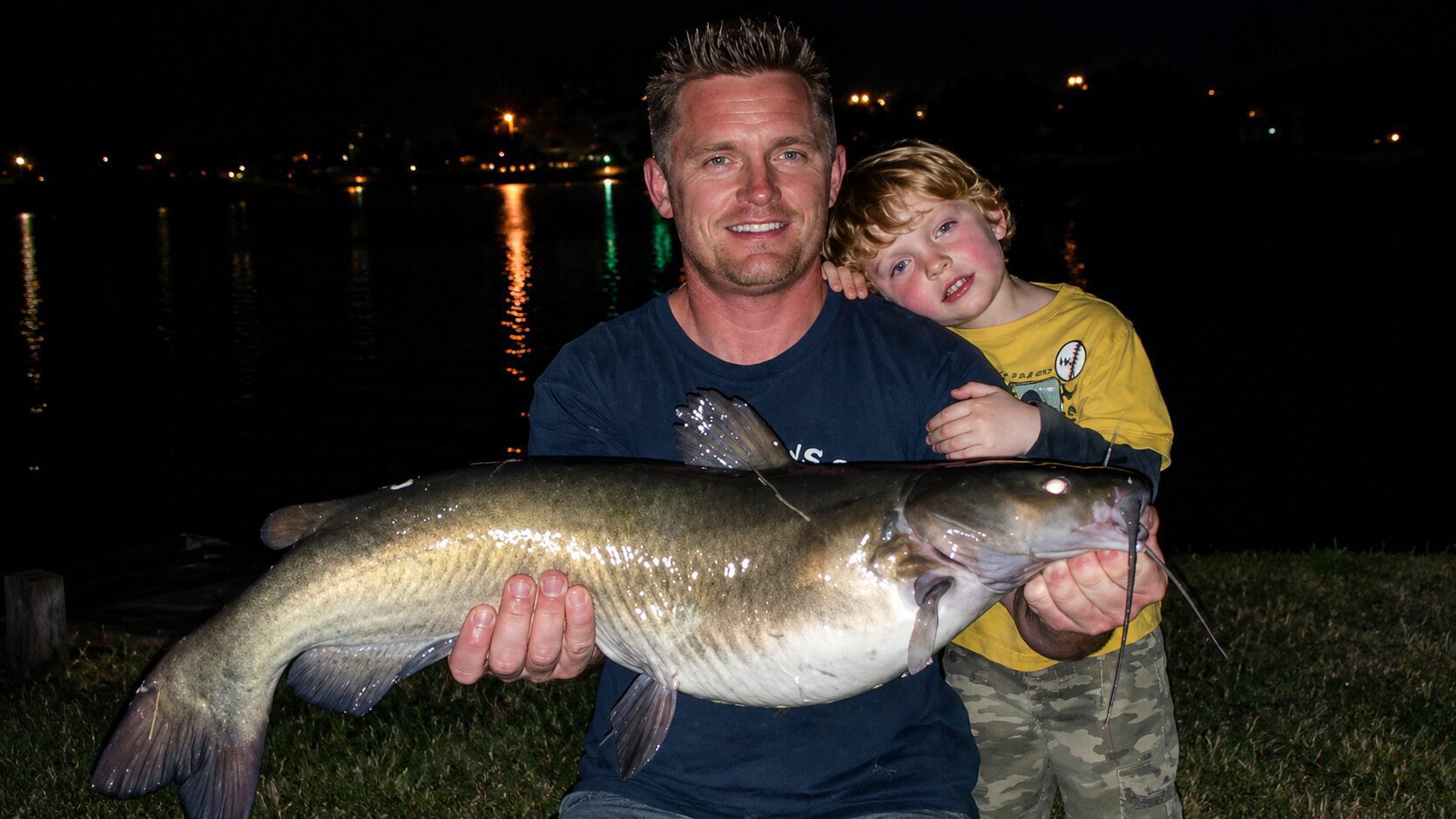 Man and child holding large fish outdoors.