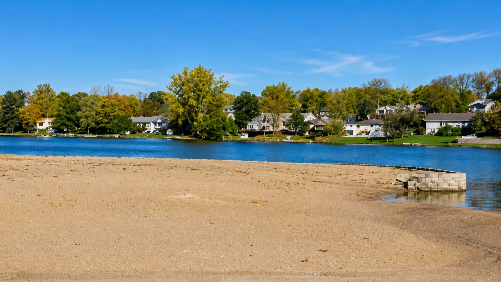 Sandy lake shore with houses and trees.