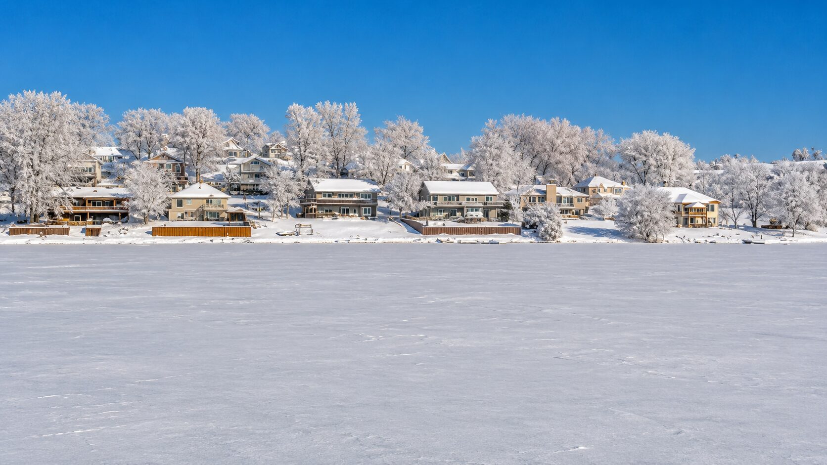 Snow-covered houses by a frozen lake.
